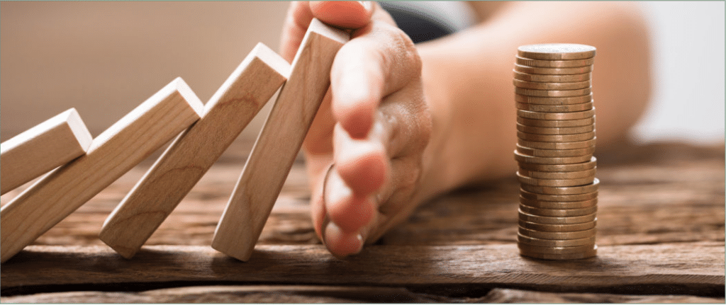 A Hand Stopping Dominoes From Falling On A Pile Of Change.